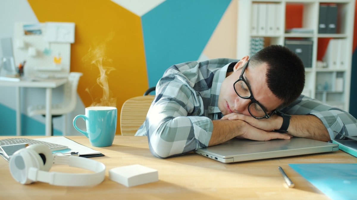 Man sleeping at desk with coffee and laptop. — a Sleep Finally guide to Tired but Wired: What the Feeling Actually Means.