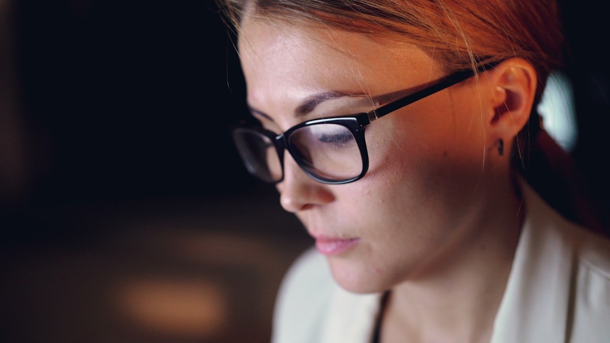 Woman wearing glasses looking intently at screen. — a Sleep Finally guide to Wear Sunglasses on the Ride Home From Nights.