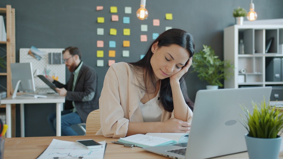 Woman resting head on hand at desk. — a Sleep Finally guide to What Cataplexy Looks Like in Daily Life.