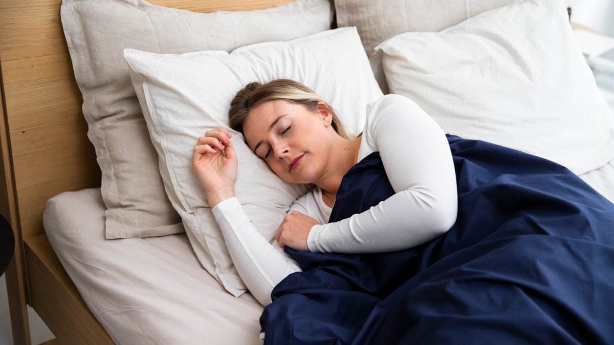 A woman sleeping on a bed with a blue blanket. — a Sleep Finally guide to What to Tell Your Doctor About Menopause Sleep.