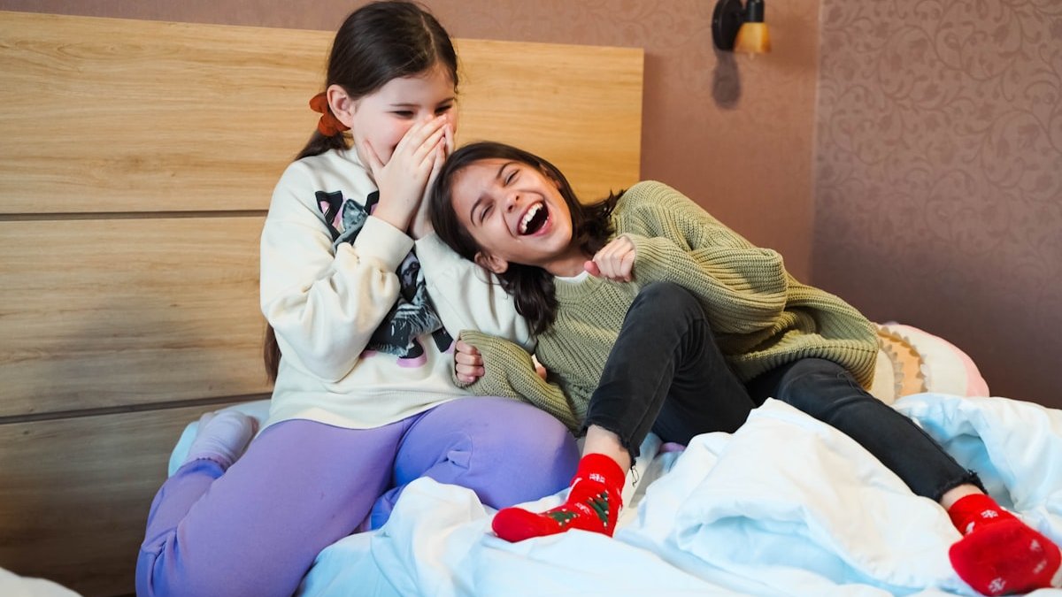 A couple of girls sitting on top of a bed. — a Sleep Finally guide to When Kids Sneak Into Your Bed at Night.
