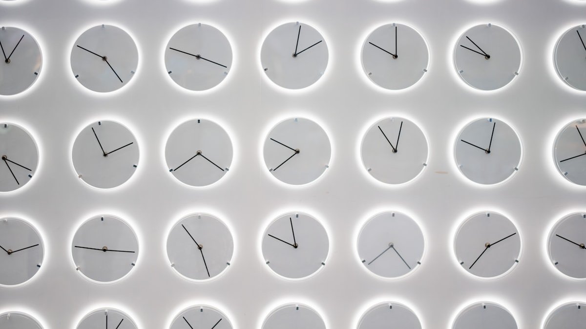 A white wall with many clocks on it. — a Sleep Finally guide to When to Get Morning Light: The First Hour Rule.