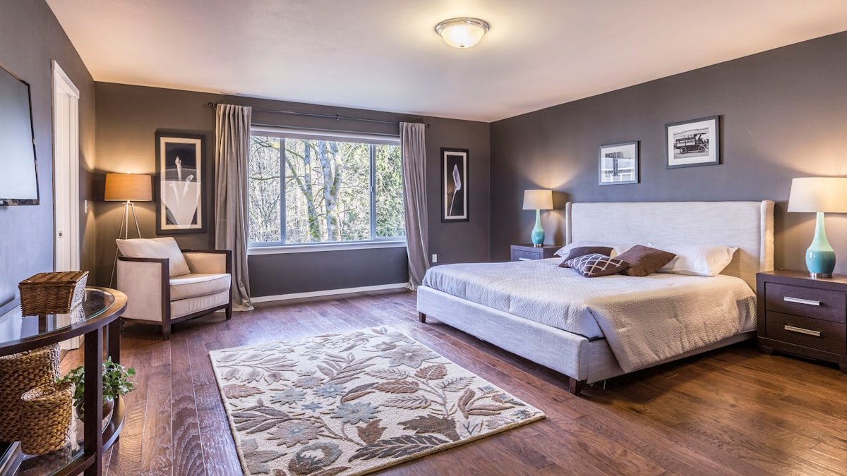 A bedroom with dark grey walls, a large bed, and a floral area rug. — a Sleep Finally guide to When Your Partner Snores: Fix the Room First.