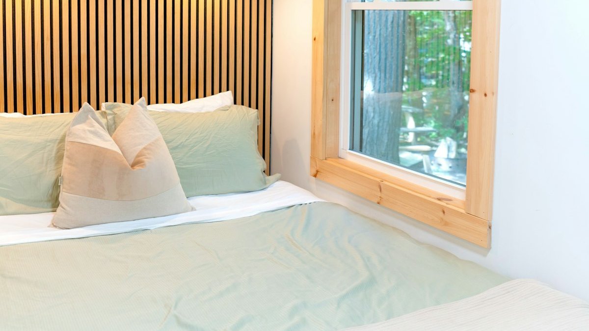 A bed with sage green bedding against a slatted wood wall in a bedroom. — a Sleep Finally guide to Where to Charge Your Phone So It Never Reaches Bed.