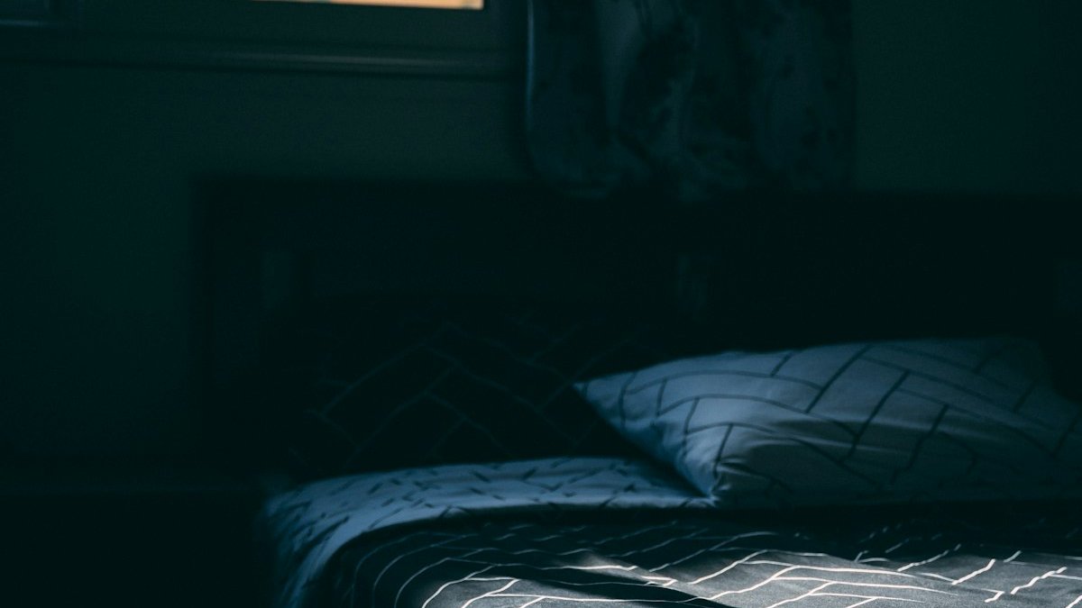 A bed sitting in a bedroom next to a window. — a Sleep Finally guide to white noise for sleep.