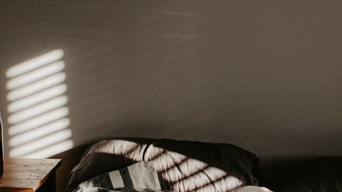A rumpled bed with striped bedding in a room with slatted light patterns. — a Sleep Finally guide to Why Arguments Before Bed Ruin Your Whole Night.