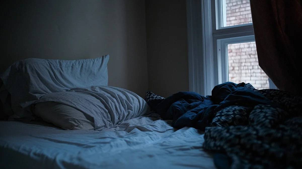 An unmade bed in a dark, quiet bedroom — a Sleep, Finally guide to Why Depression Makes You Sleep Too Much (and What Helps)